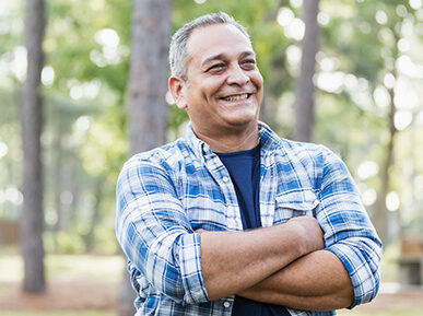 man smiling with crossed arms in a forest